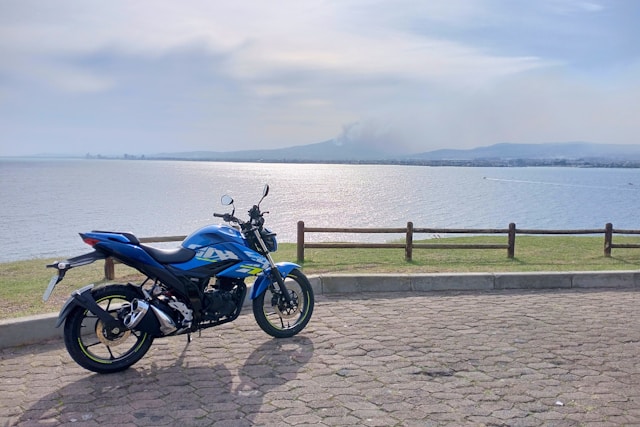 Moto di colore blu è parcheggiata su una strada lastricata, affacciata su un’ampia distesa d’acqua